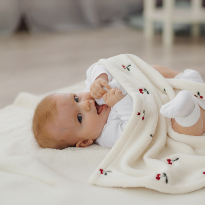 Bébé joyeux sous une couverture bébé à motif de cerises