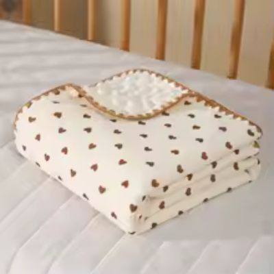 Couverture bébé avec motif de cœur posée sur un lit.