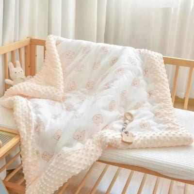 Couverture bébé avec motifs ourson disposée dans un lit en bois avec doudou lapin, montrant la texture douce et le design adorable