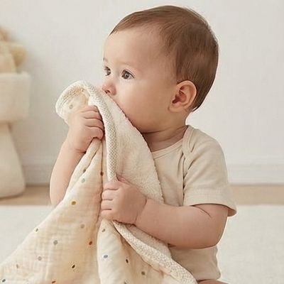 Couverture bébé beige à pois câlinée par un jeune enfant assis sur fond clair minimaliste