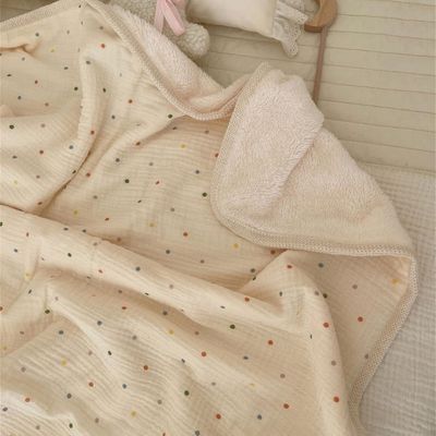 Couverture bébé beige à pois drapée sur surface blanche.