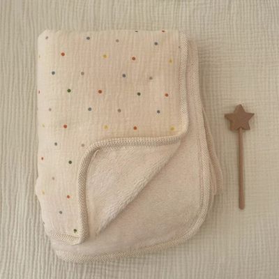 Couverture bébé beige à pois soigneusement pliée sur surface texturée blanche avec hochet en bois naturel