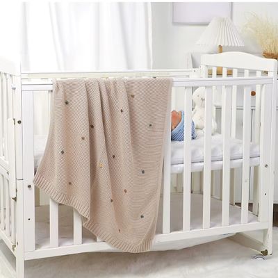  Couverture bébé beige tricotée sur lit bébé blanc avec nouveau-né endormi dans chambre lumineuse