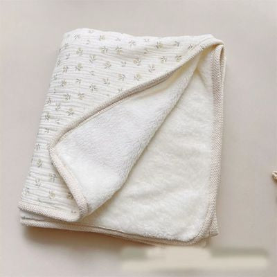 Couverture bébé blanche à motif floral  jaune délicat soigneusement pliée montrant le recto imprimé et le verso uni doux, finitions bordure beige raffinées