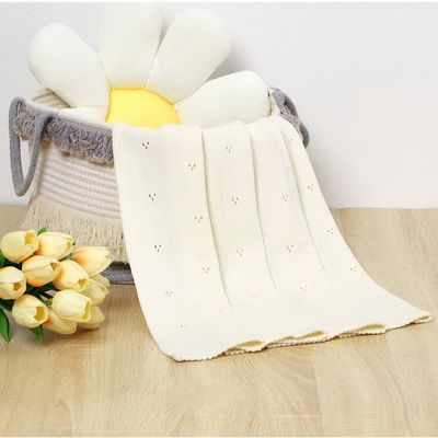 Couverture bébé douce en coton blanc crème avec broderie ajourée pliée dans panier tressé avec tulipes jaunes