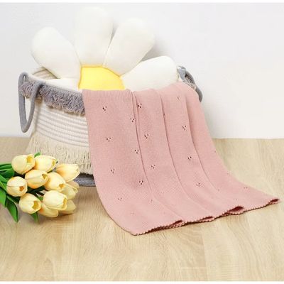 Couverture bébé douce rose poudré en coton avec broderie ajourée pliée dans panier tressé avec tulipes jaunes