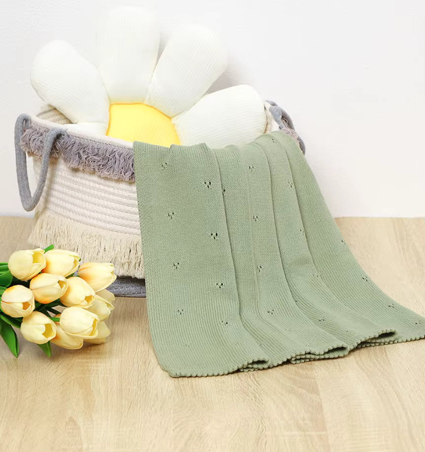 Couverture bébé douce vert sauge en coton tricoté avec broderie ajourée détail texture dans panier macramé