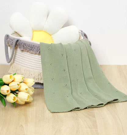 Couverture bébé douce vert sauge en coton tricoté avec broderie ajourée détail texture dans panier macramé