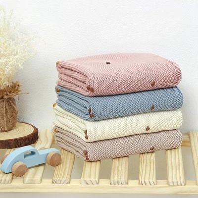Couverture bébé empilées en quatre coloris : rose, bleu, crème et beige avec détails tricot et boutons