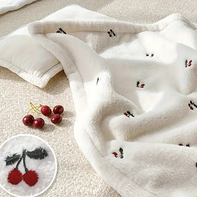 Couverture bébé sur le lit, accompagnée d’un oreiller et de cerises à proximité