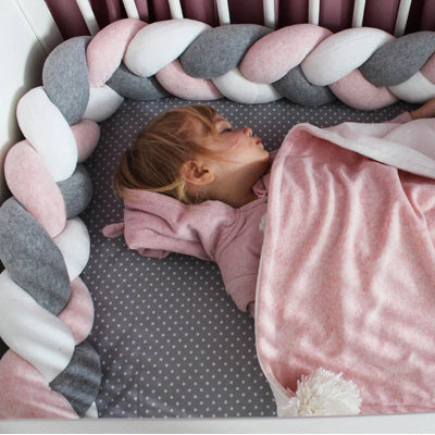 Petite fille endormie dans un lit à barreaux, entourée d’une tresse de lit décorative et sécurisante."
