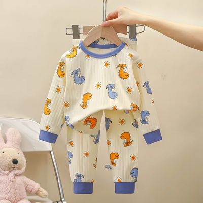 Pyjama bébé deux pièces motif dinosaures colorés avec col et poignets bleus, présenté sur cintre avec peluche ourson rose