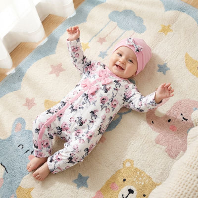 Pyjama bebe blanc à fleurs roses avec bonnet assorti, bébé souriant allongé sur tapis .