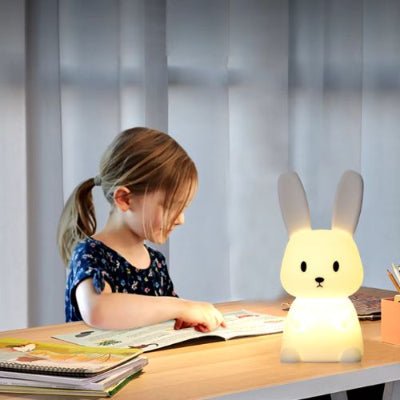 Une fillette lit un livre à son bureau, éclairée par une veilleuse bébé en forme de lapin