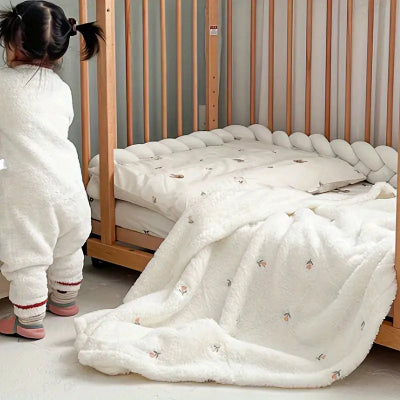  Une petite fille debout, de dos, devant un lit sur lequel est jetée une couverture bébé à motif de petites fleurs.
