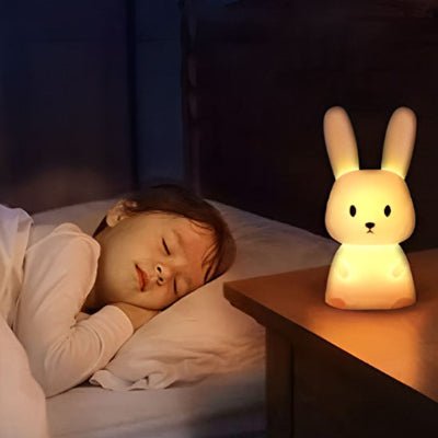 Une petite fille dort paisiblement, avec une veilleuse bébé diffusant une lumière douce posée sur sa table de chevet