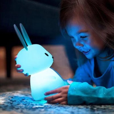 Une petite fille tient dans sa main une veilleuse bébé en forme de lapin, diffusant une lumière bleue